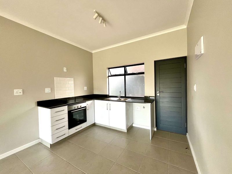 A clean, modern kitchen featuring white cabinetry, black granite countertops, a built-in oven, and neutral tiled flooring in an open-plan layout.