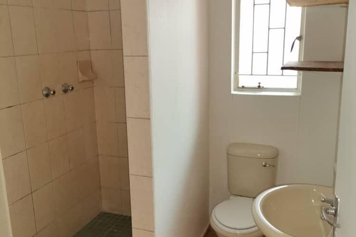 A functional bathroom featuring a walk-in shower with tiled enclosure, pedestal basin, and toilet, finished with neutral wall and floor tiles.