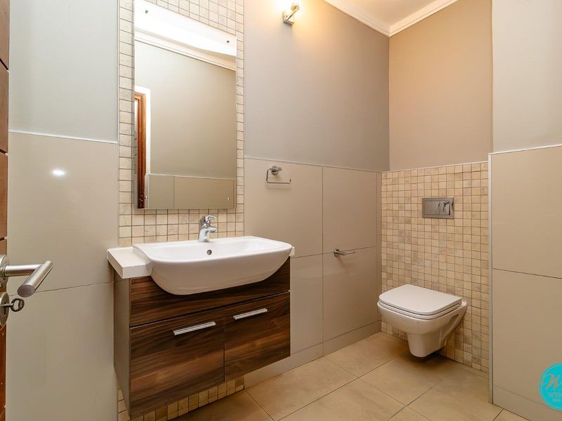 A modern, well-maintained bathroom featuring a wall-mounted vanity with a ceramic basin, a wall-mounted toilet with a concealed cistern, and neutral tiled finishes.