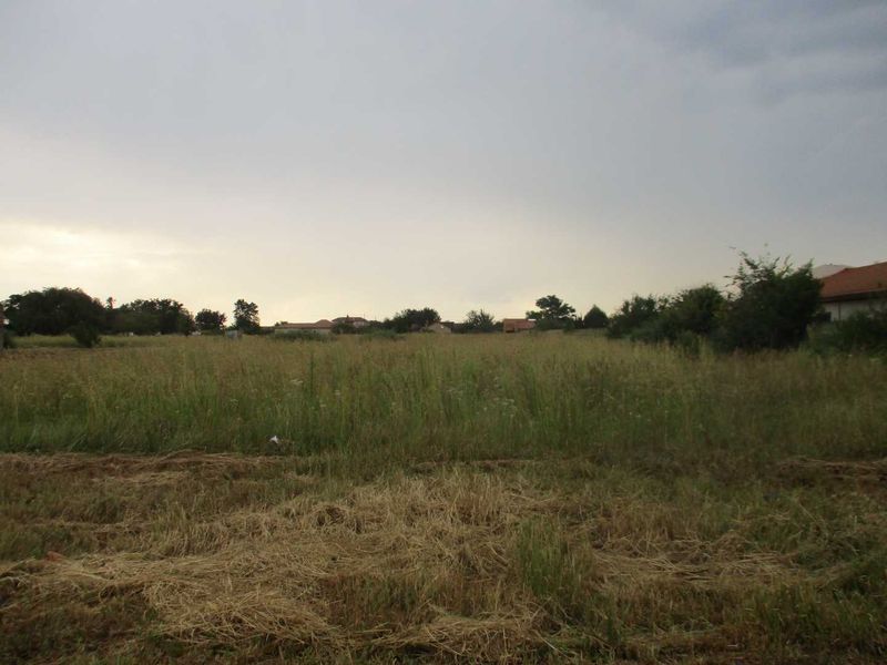 A view of a vacant residential plot featuring open grassland and surrounding neighborhood scenery.