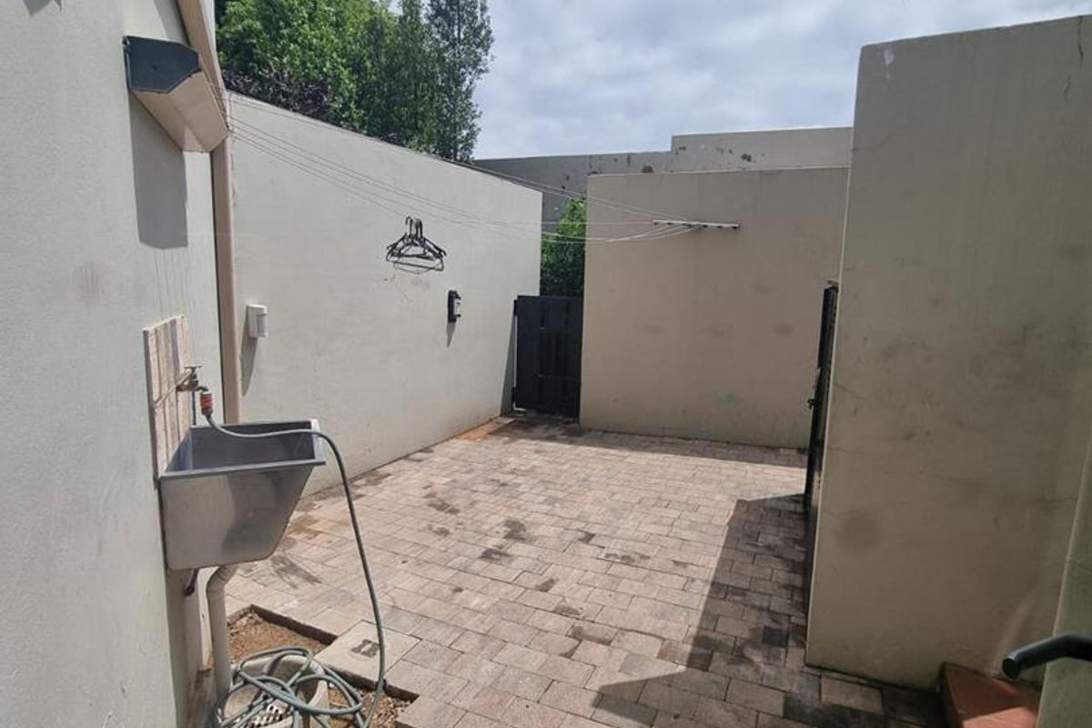 A private rear courtyard featuring paved flooring, a utility sink, and wall-mounted clothesline, offering a functional outdoor utility space.