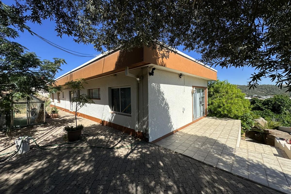 A view of the rear exterior of the house featuring a paved patio area, textured wall finish, and a small greenhouse structure.
