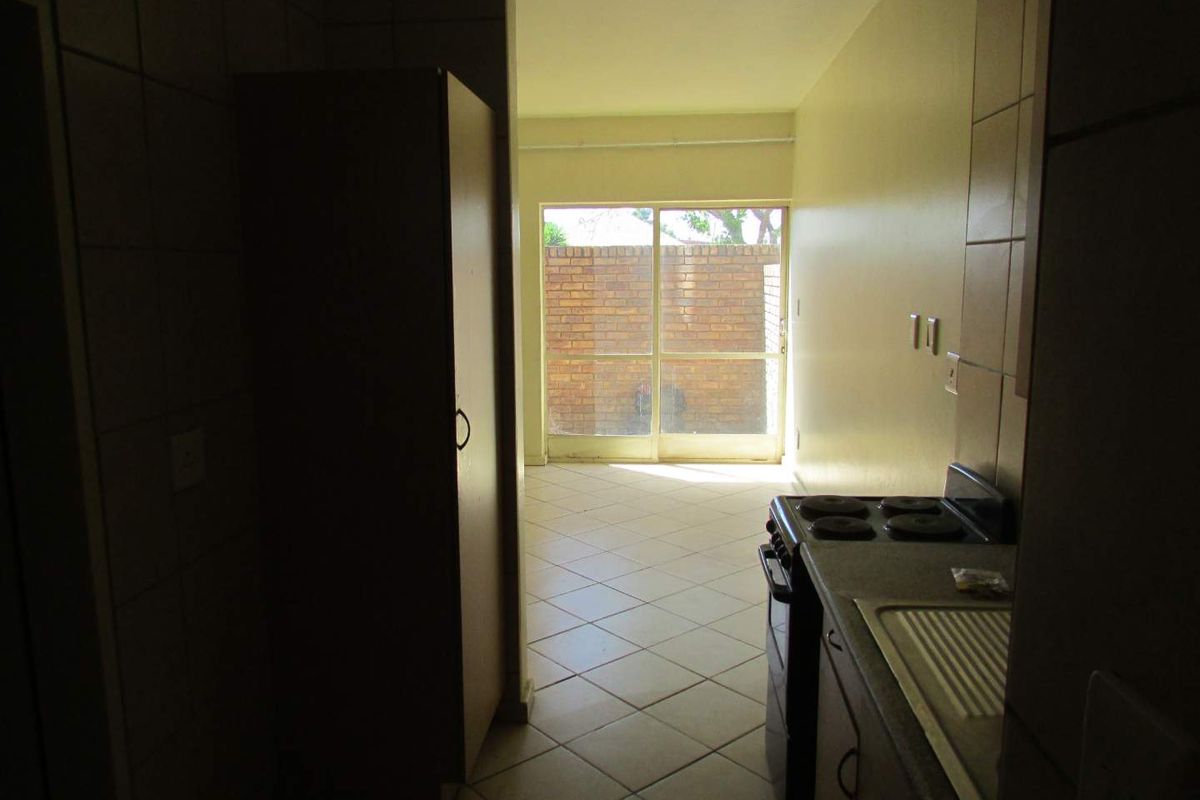 A compact kitchen area featuring tiled floors, built-in cabinetry, and a freestanding stove, leading directly to an outdoor patio space.