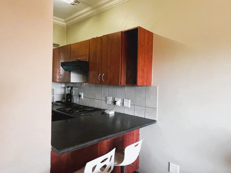 A compact kitchen featuring wooden cabinetry, a dark laminate countertop, tiled backsplash, and an integrated extractor fan, showing signs of wear and missing cabinetry.