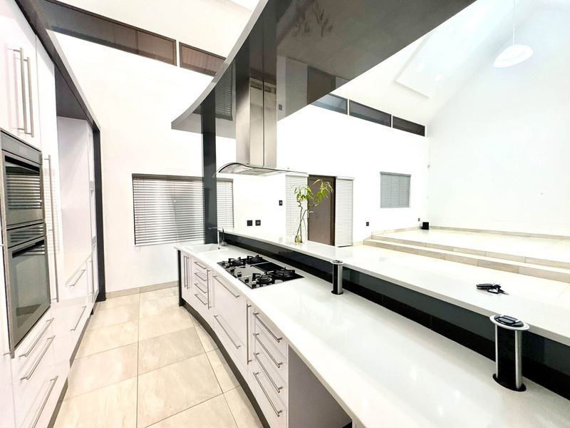 Modern, spacious kitchen featuring high vaulted ceilings, sleek white cabinetry, stone countertops, a gas hob, and integrated appliances in an open-plan layout.