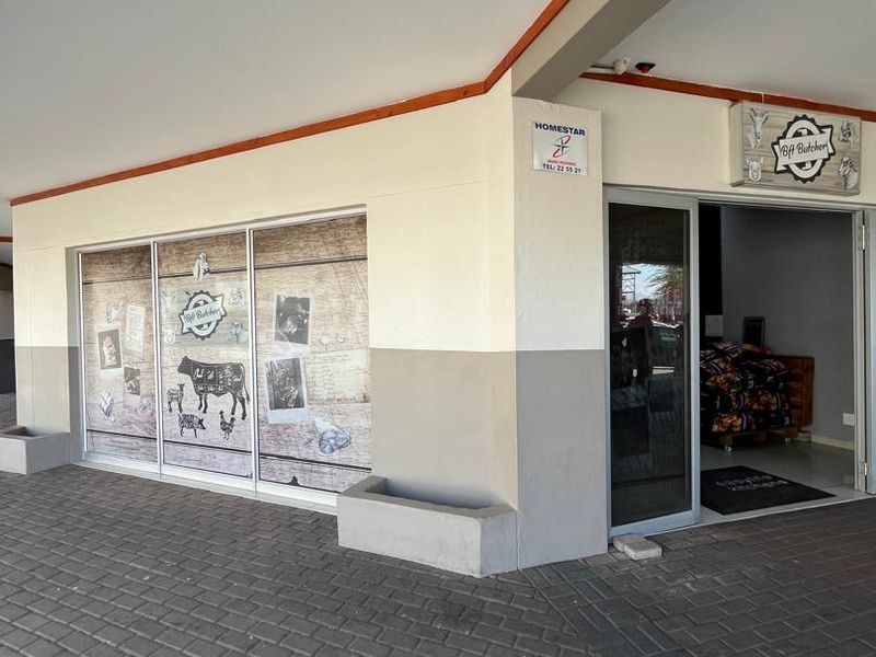 Front entrance of a commercial business unit featuring a paved walkway, covered porch area, and glass storefront display.