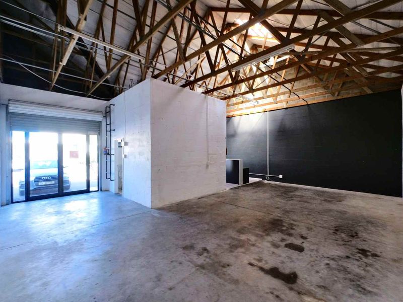 Spacious industrial utility area featuring exposed timber roof trusses, concrete flooring, and a roller shutter door for convenient access.