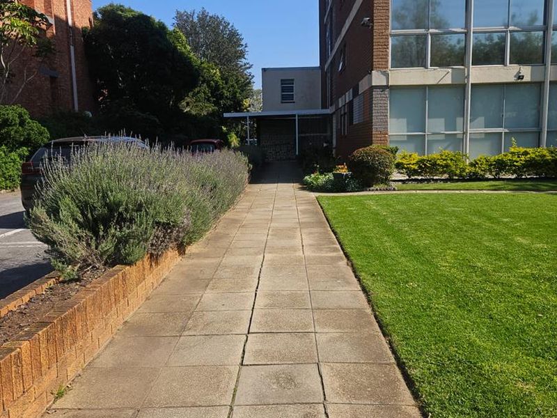 Exterior view of the apartment building featuring a paved walkway, manicured lawn, and brick facade with large windows.