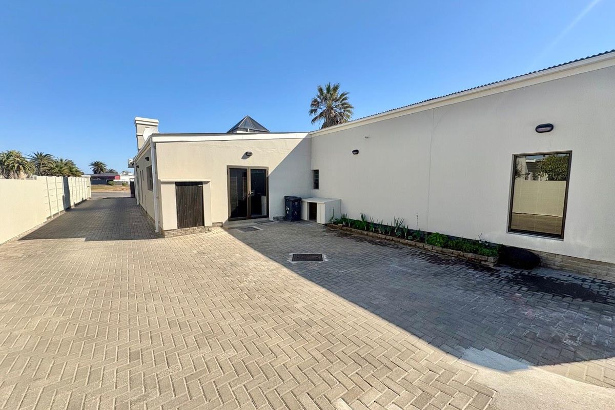 A paved rear courtyard area featuring a clean exterior facade, external lighting, and a skylight, providing a functional outdoor space.