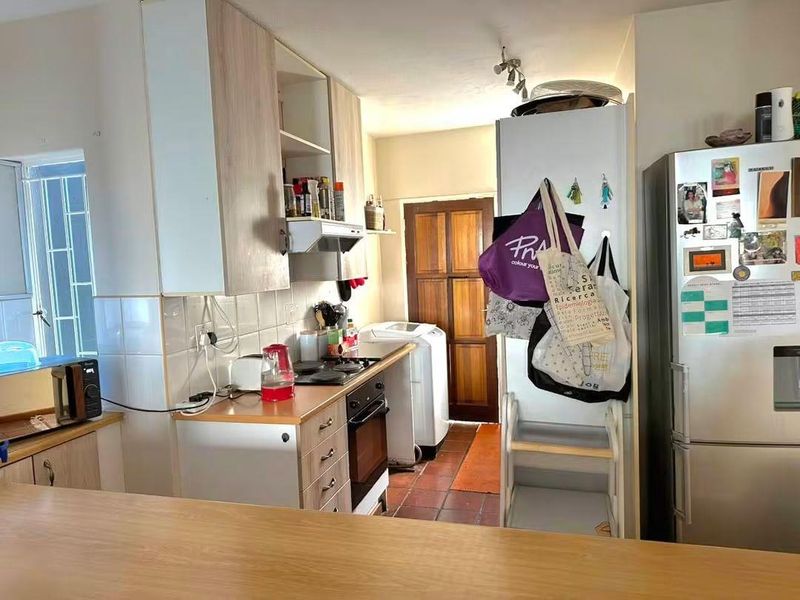 A functional kitchen featuring built-in cabinetry, an electric hob, oven, and extractor fan, with tiled flooring and a tiled backsplash.