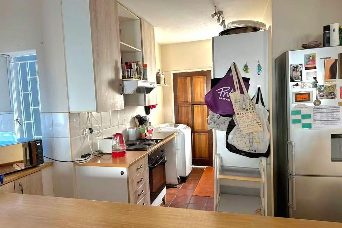 A functional kitchen featuring built-in cabinetry, an electric hob, oven, and extractor fan, with tiled flooring and a tiled backsplash.