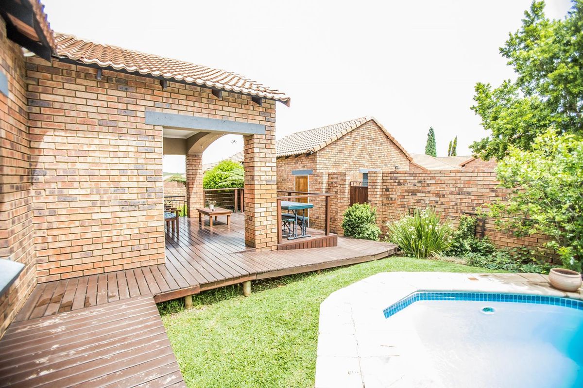 Rear exterior view featuring a covered brick patio, timber decking, and a swimming pool set within a private garden area.