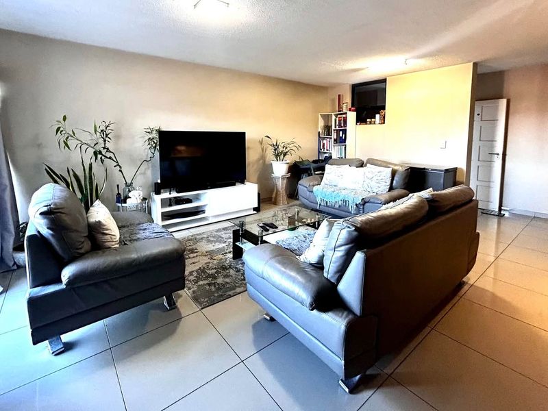 A spacious living room featuring large format floor tiles, neutral wall tones, and a sliding glass door providing access to the exterior.