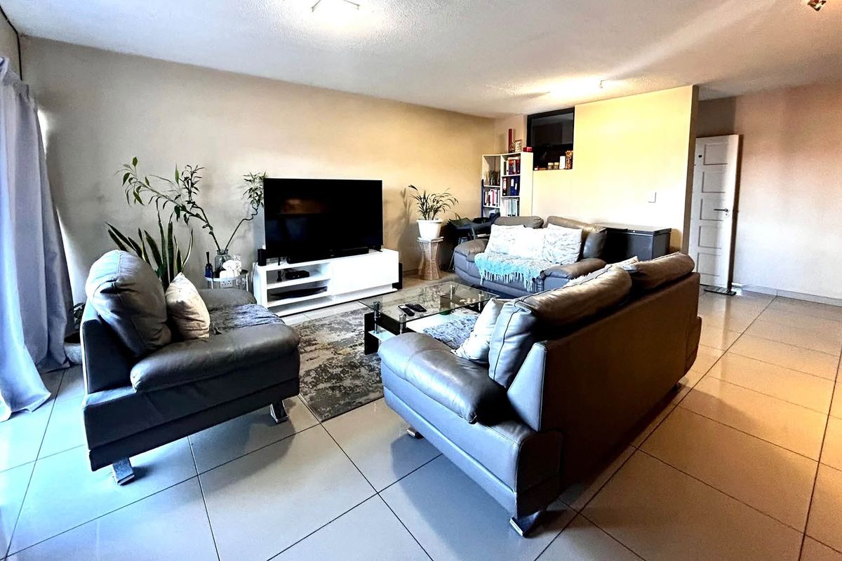 A spacious living room featuring large format floor tiles, neutral wall tones, and a sliding glass door providing access to the exterior.