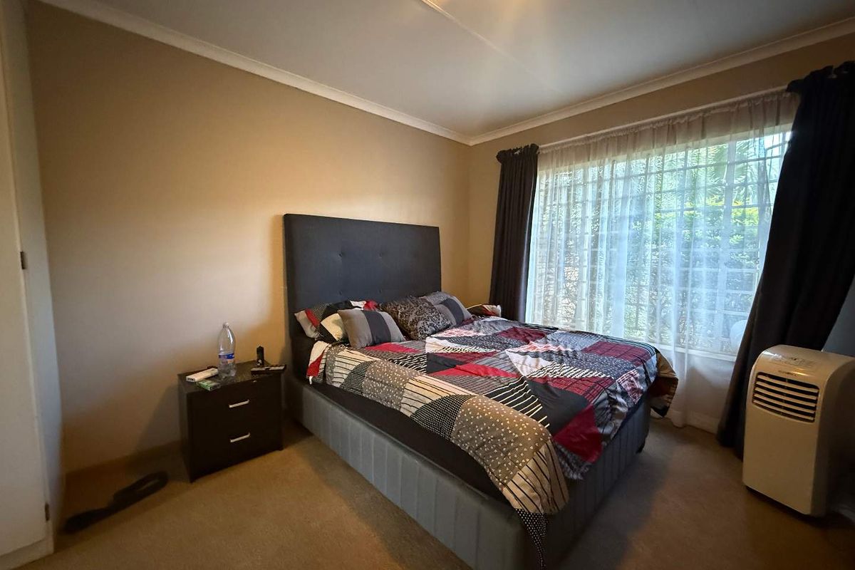 A functional bedroom featuring neutral wall tones, carpeted flooring, and a window fitted with security bars, offering a comfortable and private living space.