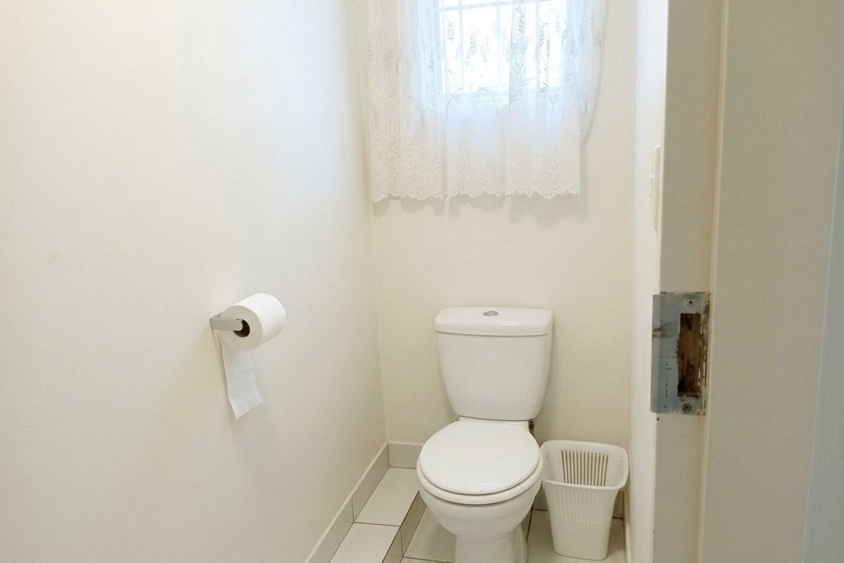 A compact, functional bathroom featuring a white toilet, tiled flooring, and a window with security bars.