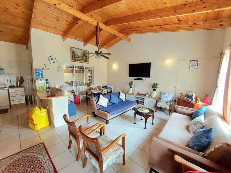 Spacious open-plan living and kitchen area featuring high exposed timber beam ceilings, ceramic tiled flooring, and a functional breakfast bar layout.