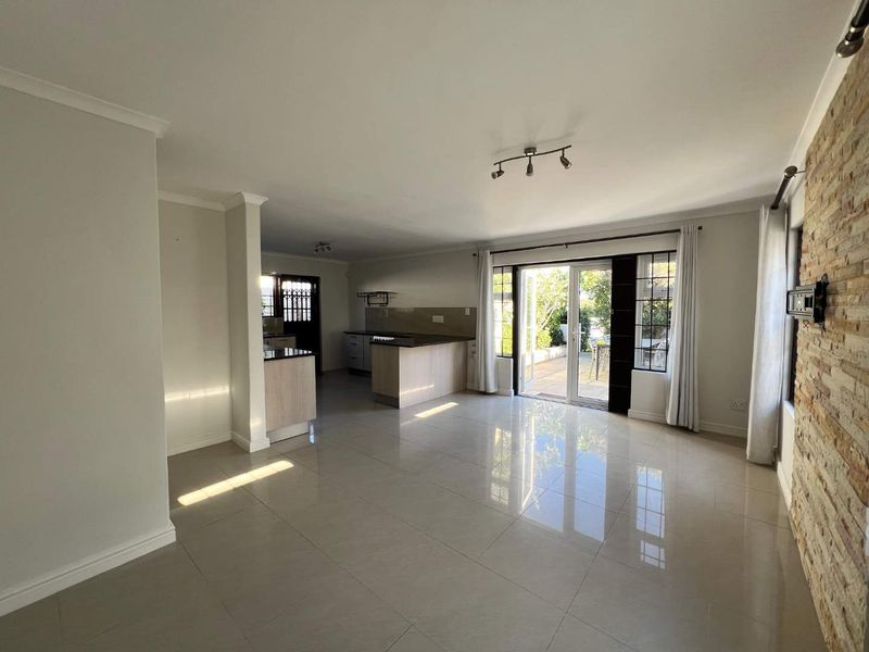 Spacious open-plan living area featuring tiled floors, a stone accent wall, and a functional kitchen with an island, leading out to a patio.