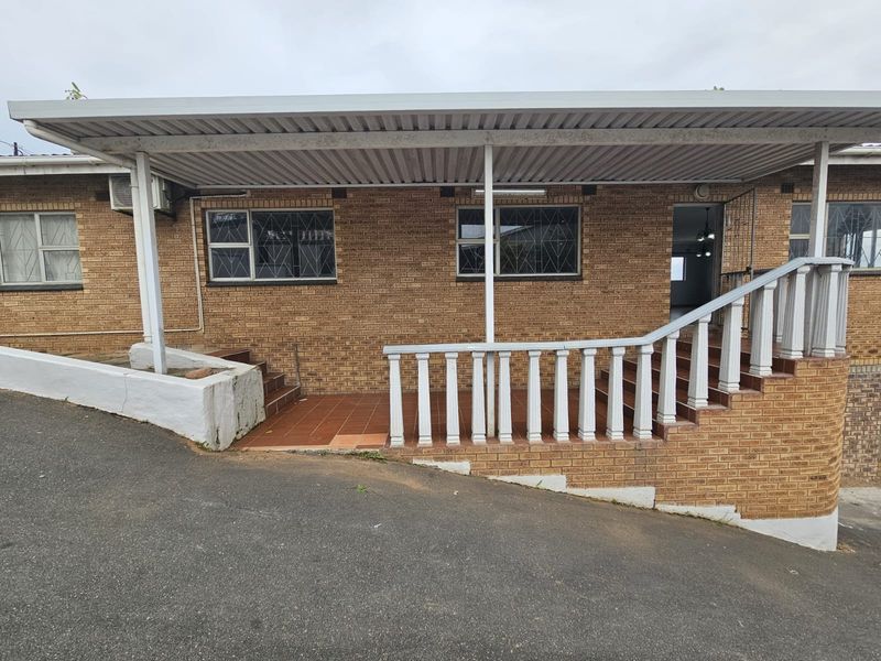 Front exterior view of a brick house featuring a covered patio area with a balustrade and tiled steps leading to the entrance.