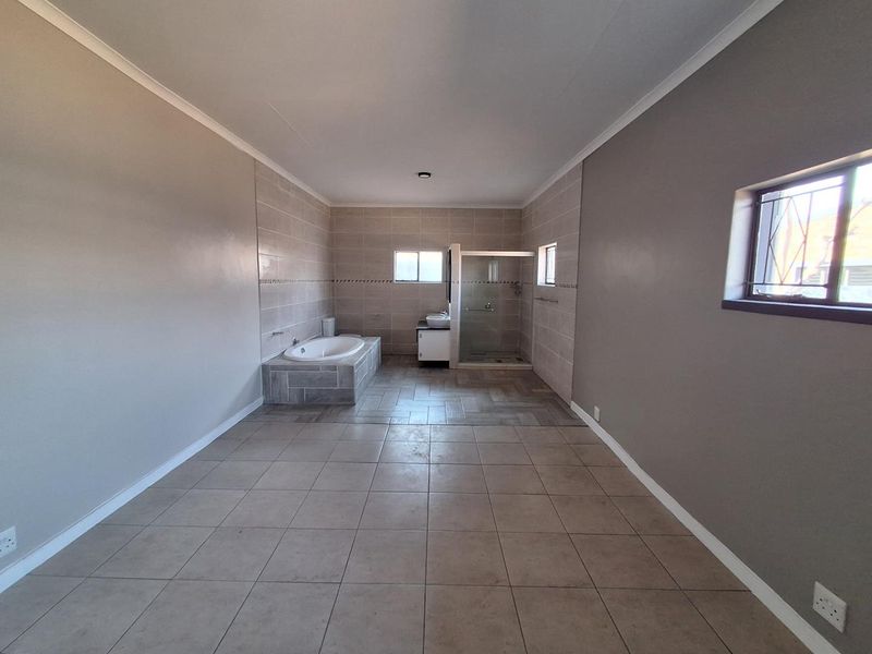 Spacious bathroom featuring a built-in bathtub, separate glass shower enclosure, and vanity cabinet with neutral floor and wall tiling.