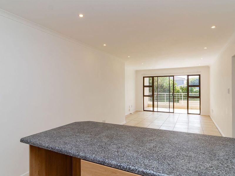 Spacious open-plan living area featuring tiled floors, recessed lighting, and large sliding glass doors leading to a private balcony.