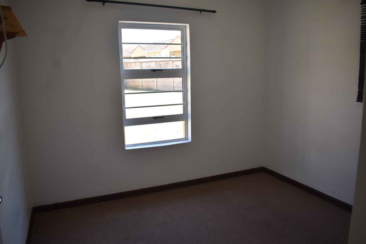 A vacant bedroom featuring neutral carpeting, plain walls, and a window fitted with security bars.