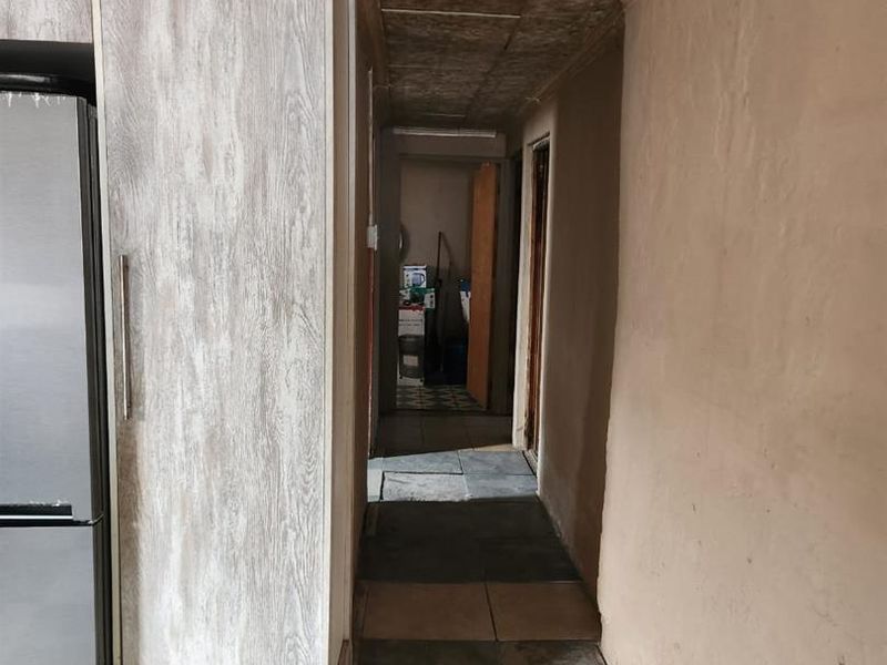 A narrow hallway featuring tiled flooring and textured ceiling tiles, leading towards other areas of the home.