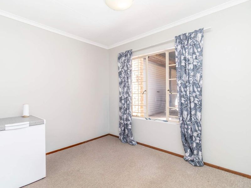 A simple, neutral-toned bedroom featuring carpeted flooring and a large window, providing a blank canvas for personalization.