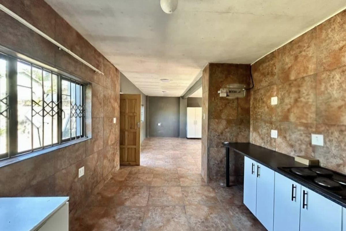 An empty kitchen area featuring tiled walls, built-in cabinetry with a hob, and tiled flooring, offering a blank canvas for renovation.