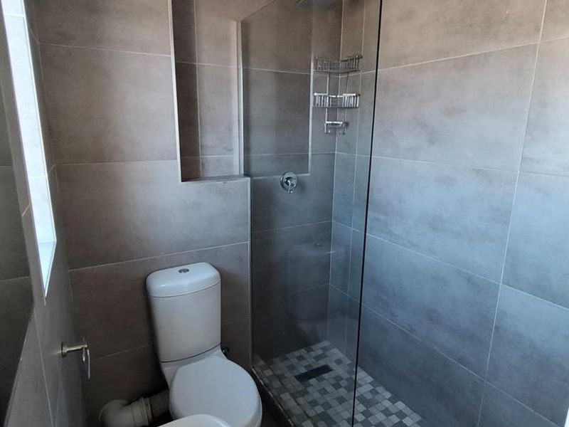 Modern bathroom featuring a walk-in shower with glass screen, mosaic tile flooring, neutral wall tiles, a pedestal basin, and a standard toilet.