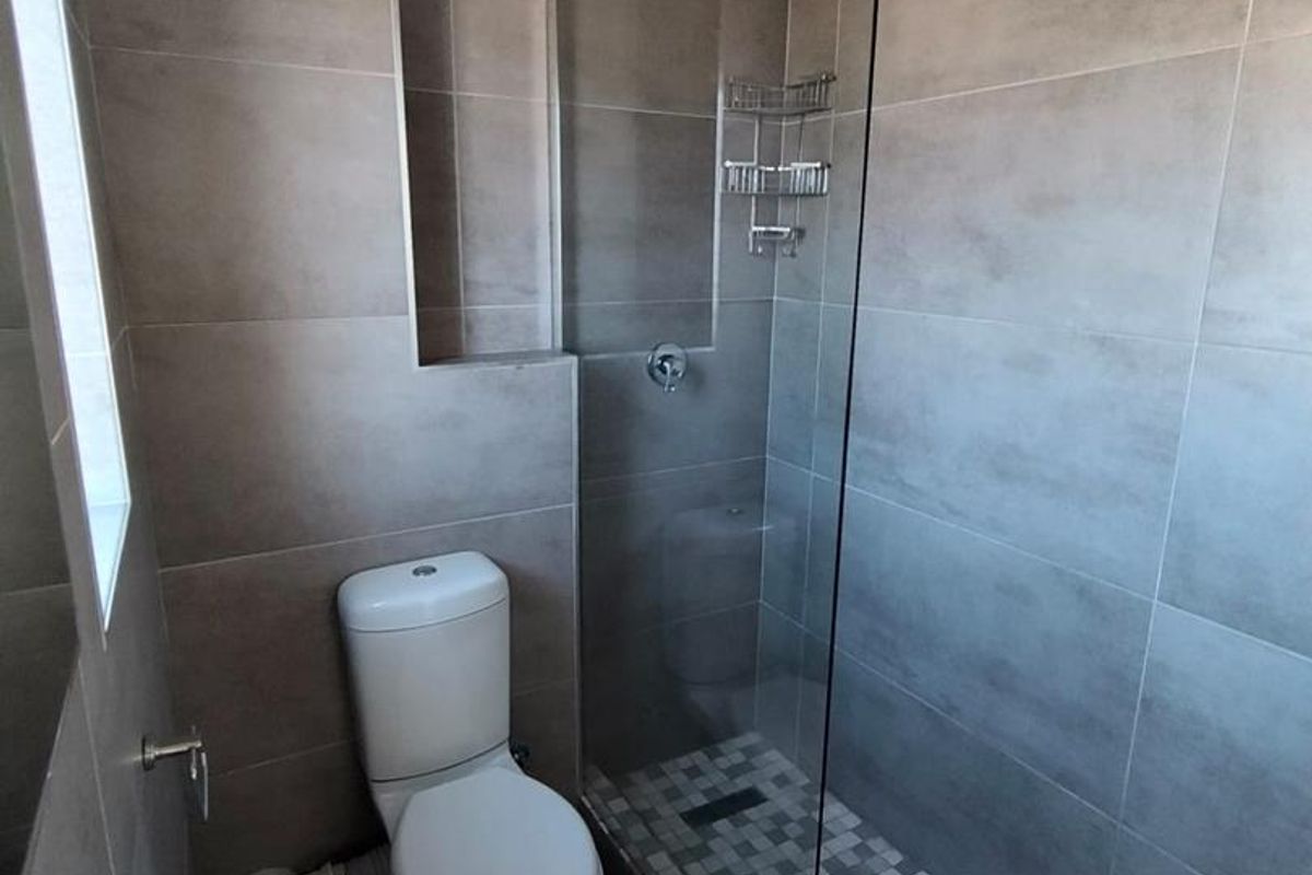 Modern bathroom featuring a walk-in shower with glass screen, mosaic tile flooring, neutral wall tiles, a pedestal basin, and a standard toilet.