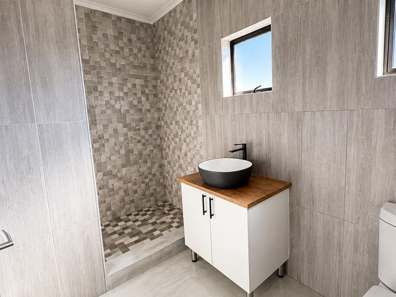 Modern bathroom featuring a walk-in shower with mosaic tiling, a contemporary vanity with a vessel sink, and neutral wood-look wall tiles.