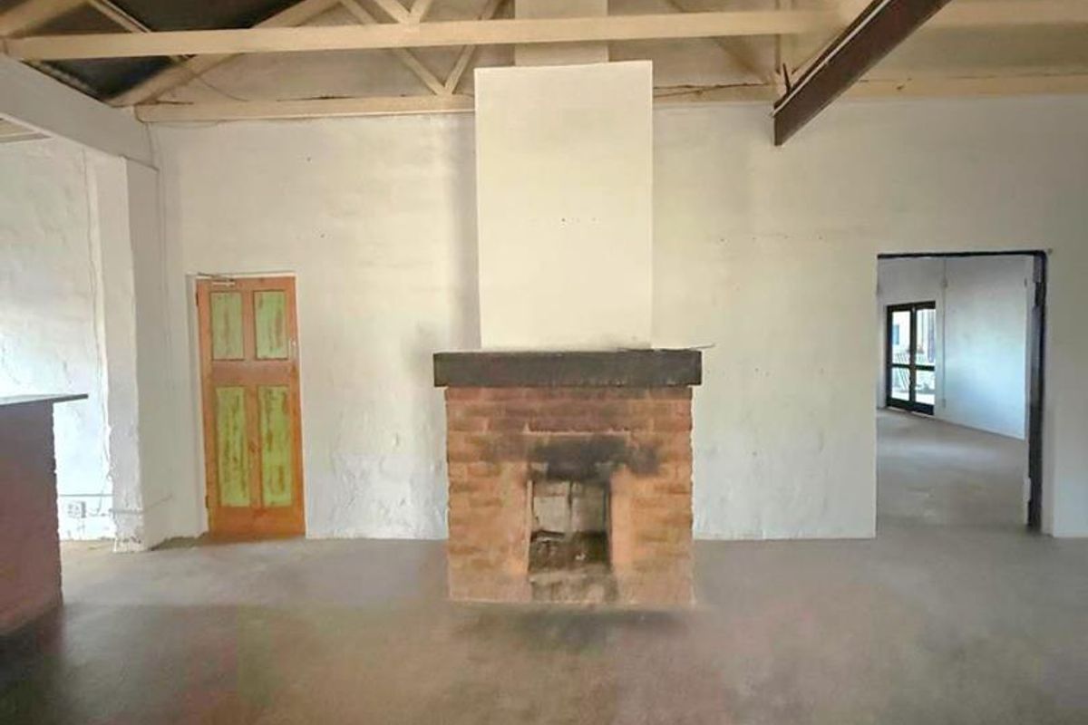 Spacious living area featuring exposed roof trusses, a central brick fireplace, and concrete flooring, offering a blank canvas for renovation.