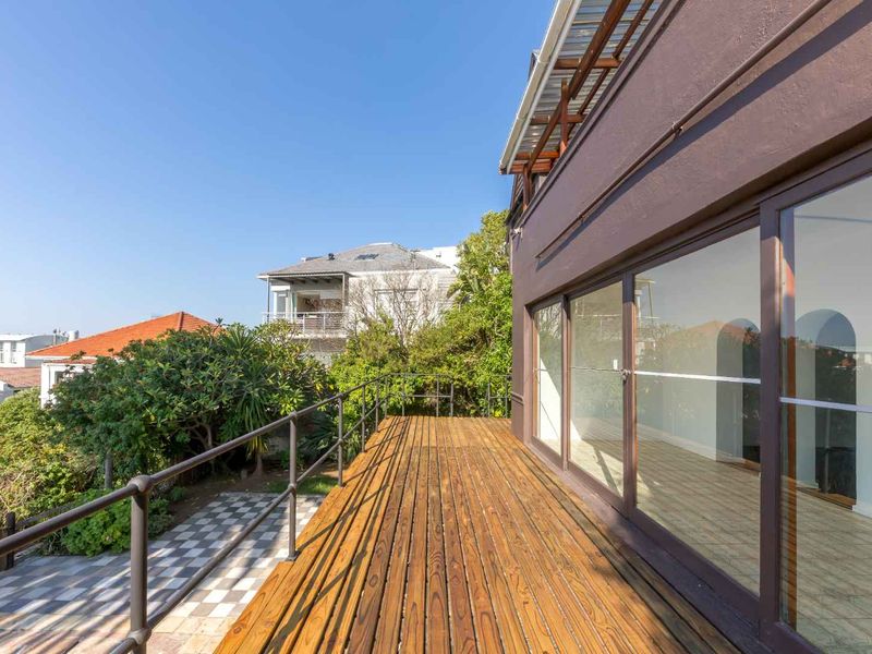 A spacious wooden balcony featuring metal railings and large sliding glass doors, offering an elevated outdoor space with views of the surrounding garden.