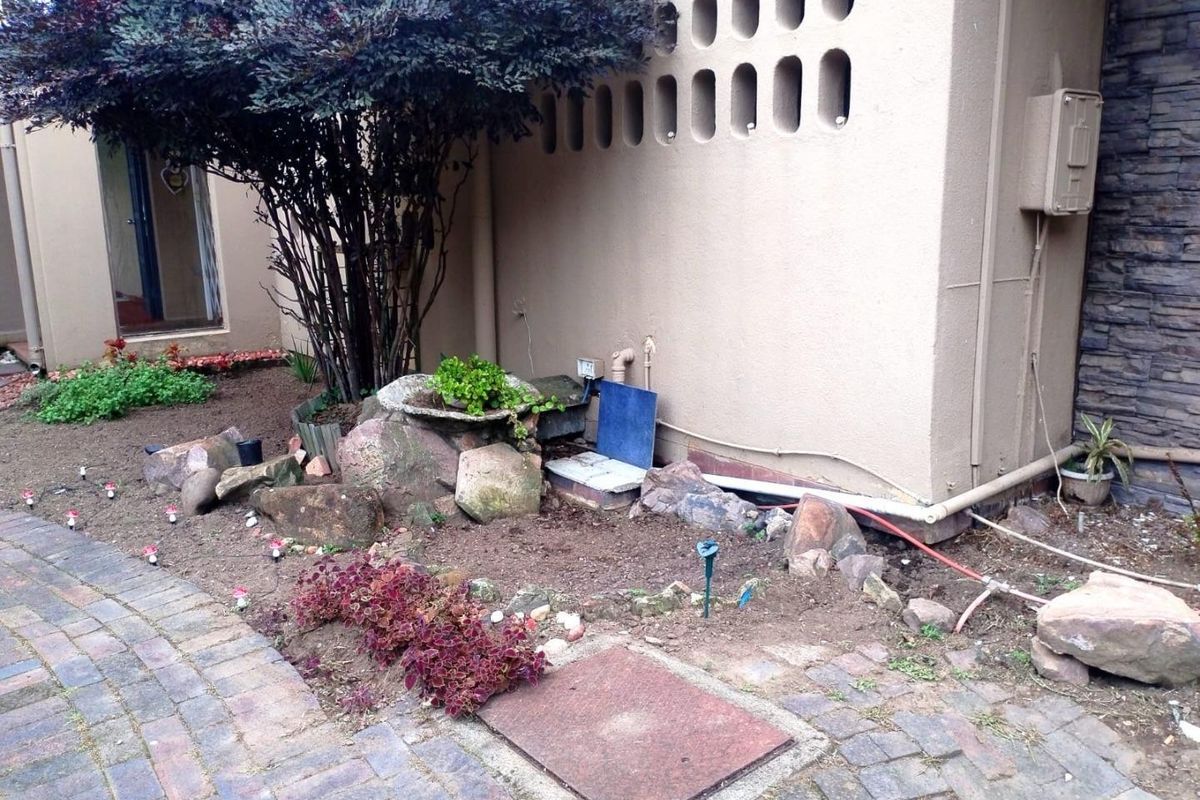 A rear exterior area featuring brick paving, stone landscaping, and a decorative breeze block wall section with visible external utility connections.
