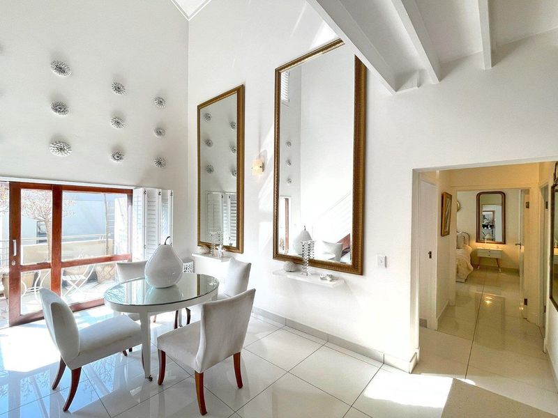 Bright living area featuring high vaulted ceilings with exposed beams, polished tile flooring, and large sliding glass doors leading to an outdoor balcony.