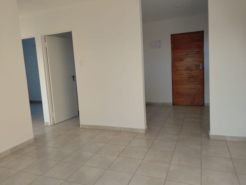 A bright, empty hallway featuring neutral tiled flooring and a solid wooden door, providing a clean and versatile transition space within the home.