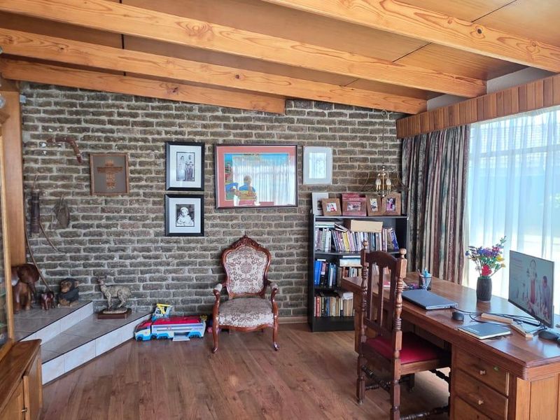 A living area featuring exposed timber ceiling beams, a rustic brick feature wall, and laminate flooring, offering a warm and traditional aesthetic.