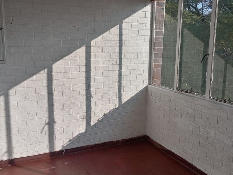 An empty, sunlit enclosed balcony or sunroom featuring painted brick walls, large windows, and a painted concrete floor.