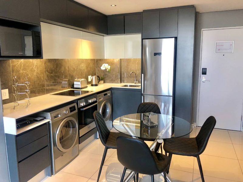 Modern open-plan kitchen featuring sleek dark and white cabinetry, stone countertops, marble-look splashback, and integrated appliances, seamlessly flowing into a dining area.