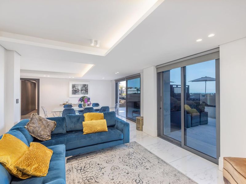 Spacious open-plan living and dining area featuring high-end marble flooring, recessed ceiling lighting, and large sliding glass doors leading to an outdoor patio.