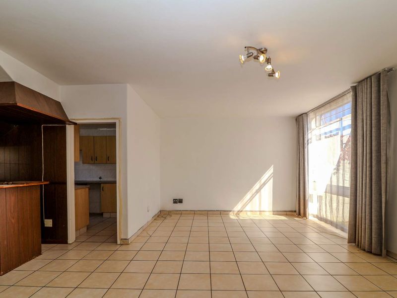An open-plan living area featuring tiled flooring, a built-in breakfast bar, and direct access to an outdoor space through a large sliding glass door.