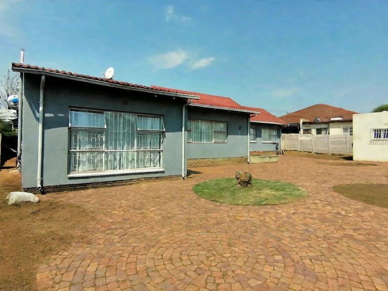 Rear view of the house featuring a large paved courtyard, tiled roof, and secure window bars, set within a walled perimeter.