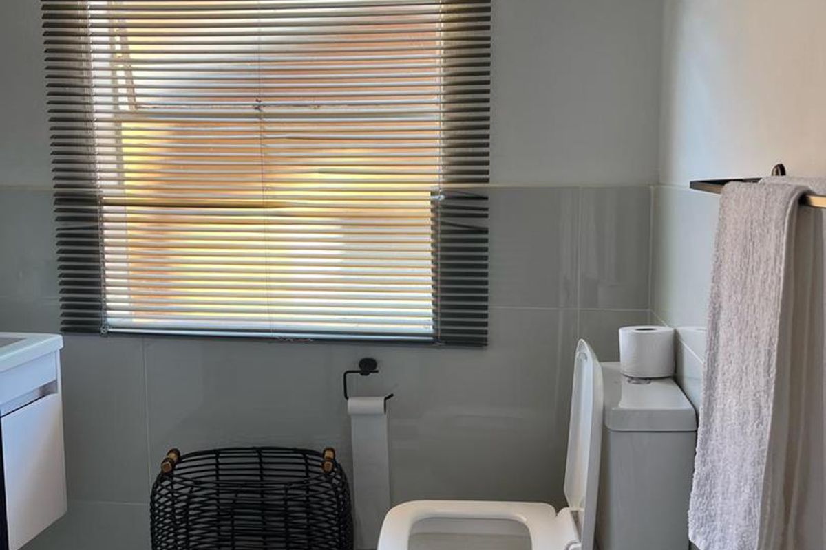 A clean, modern bathroom featuring tiled walls, a white toilet, and a window with fitted blinds.
