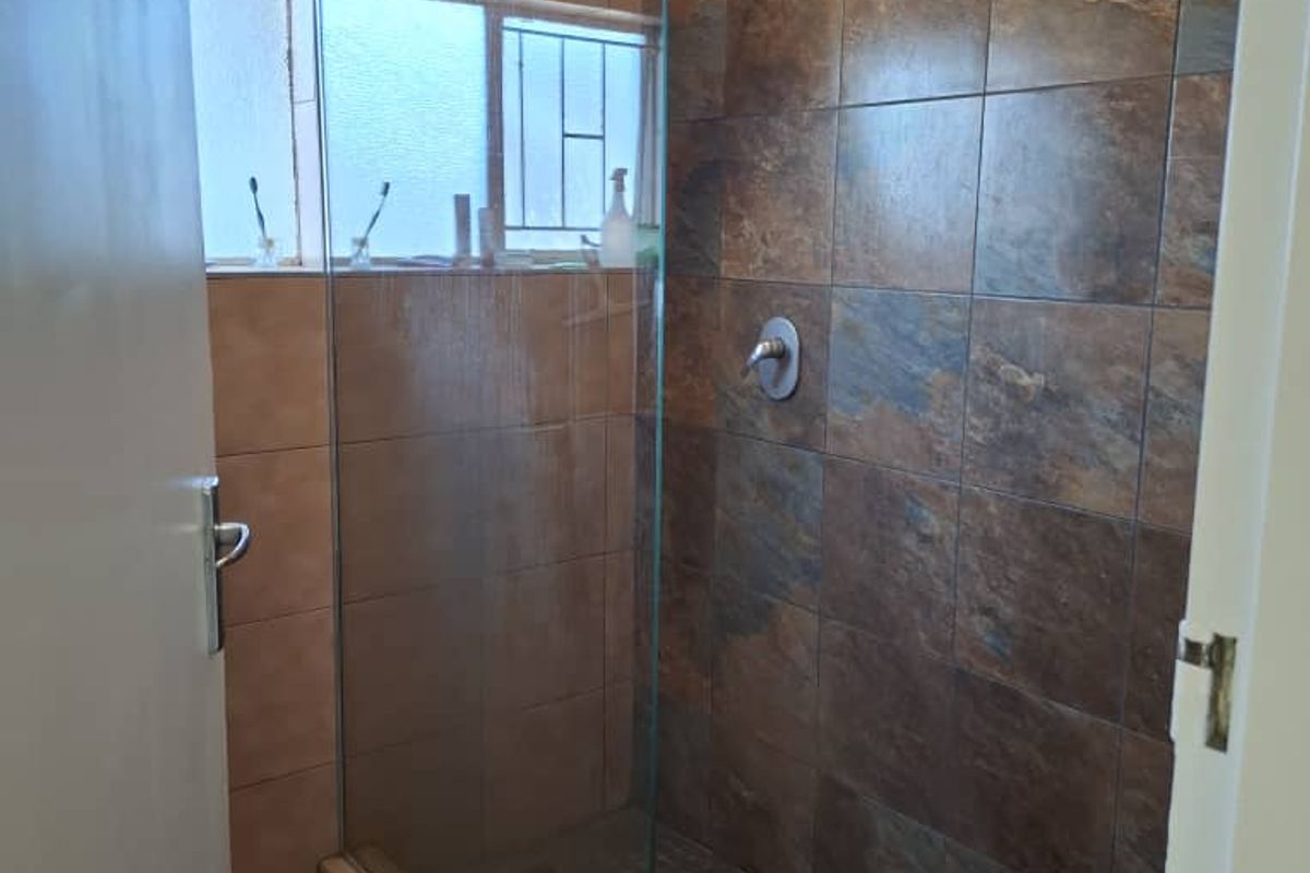 A modern walk-in shower featuring a glass partition, rainfall showerhead, and textured stone-look wall tiling.