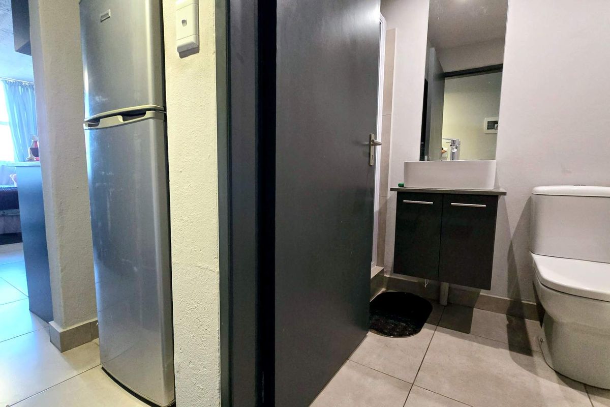 A compact bathroom featuring a modern vessel sink with vanity cabinet, wall-mounted mirror, and a standard toilet with tiled flooring.