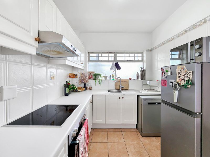 A functional kitchen featuring white cabinetry, an electric cooktop, built-in oven, stainless steel sink, and tiled flooring with a neutral backsplash.