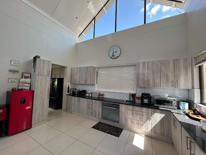Modern kitchen featuring light wood-grain cabinetry, granite countertops, built-in oven, and high vaulted ceilings with clerestory windows providing ample natural light.