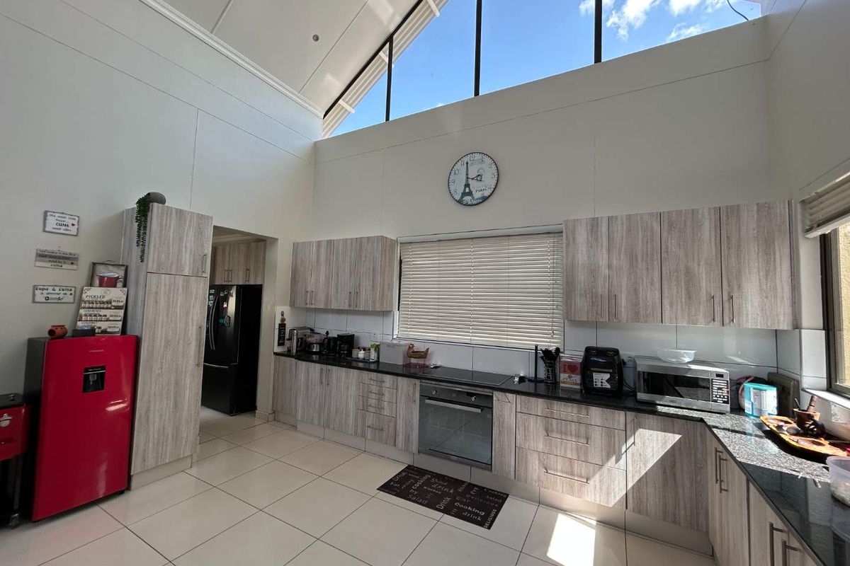 Modern kitchen featuring light wood-grain cabinetry, granite countertops, built-in oven, and high vaulted ceilings with clerestory windows providing ample natural light.