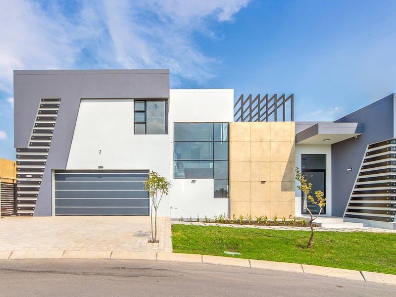 A modern, architecturally designed double-story house featuring a sleek facade, stone cladding, large glass windows, and a paved driveway with a double garage.